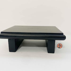 May include: A rectangular black wooden display stand with a smooth, flat top surface and two sturdy, vertical support legs. The stand features a clean, low-profile design with rounded edges along the front, showcasing a solid black finish.
