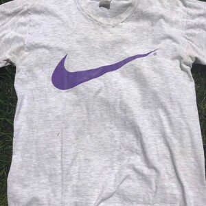 May include: A grey t-shirt with a purple Nike swoosh logo.