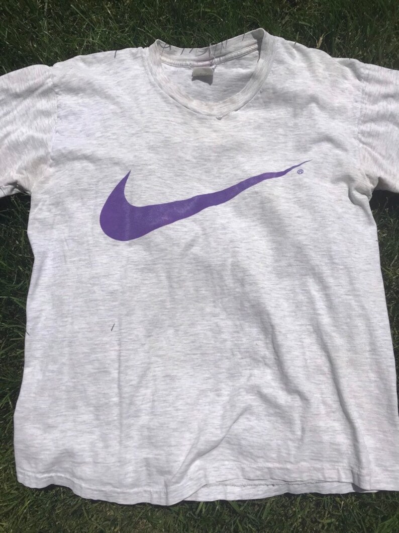May include: A grey t-shirt with a purple Nike swoosh logo.