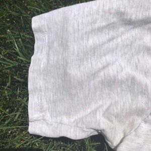 May include: A close-up of the grey fabric of a t-shirt. The fabric is soft and has a slight texture.