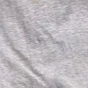 May include: A close-up of a grey, textured fabric with a small hole in the centre.