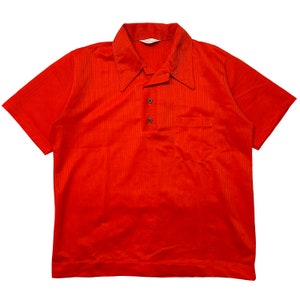 May include: A red short-sleeved polo shirt with a button-up collar and a single pocket on the left chest.