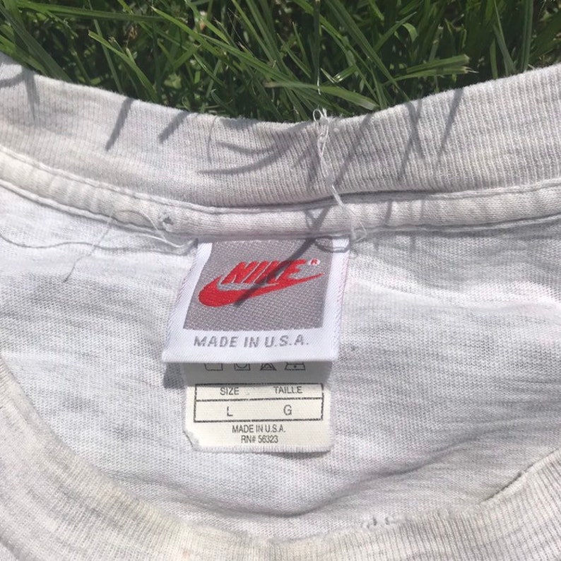 May include: White t-shirt with a grey Nike tag that says "Made in U.S.A." and a size tag that says "Size L, Taille G, Made in U.S.A., RN# 56323"