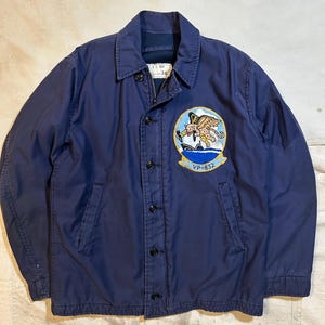 Op de afbeelding: Marineblauwe jas met een knoopsluiting en een kraag. De jas heeft een patch op de borst met een kleurrijk embleem en de tekst "VP-832". De jas heeft twee voorzakken en een label met het nummer "16".