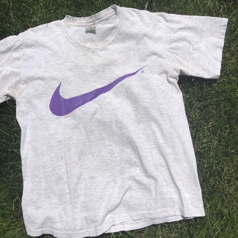May include: A vintage grey t-shirt with a purple Nike swoosh logo.