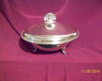 Può includere: Un piatto da portata in argento con coperchio e tre piedi. Il coperchio ha un design decorativo a conchiglia.