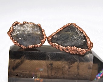 May include: A pair of earrings featuring raw, grey, crystal stones wrapped in copper wire. The stones are irregular in shape and have a natural, rough texture.