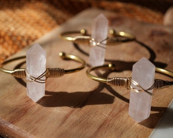 May include: Three gold wire wrapped bracelets with clear quartz crystal points. The bracelets are on a wooden surface.