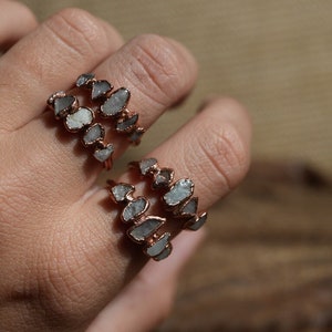 May include: Two rings made of copper wire with raw, clear quartz stones set in the wire. The rings are stacked on a finger.