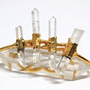 K&ouml;nnte beinhalten: Goldring mit f&uuml;nf klaren Quarzkristallen, die in Gold gefasst sind. Der Ring besteht aus einem d&uuml;nnen Goldband und die Kristalle sind so gefasst, dass sie aus dem Band herauswachsen scheinen.