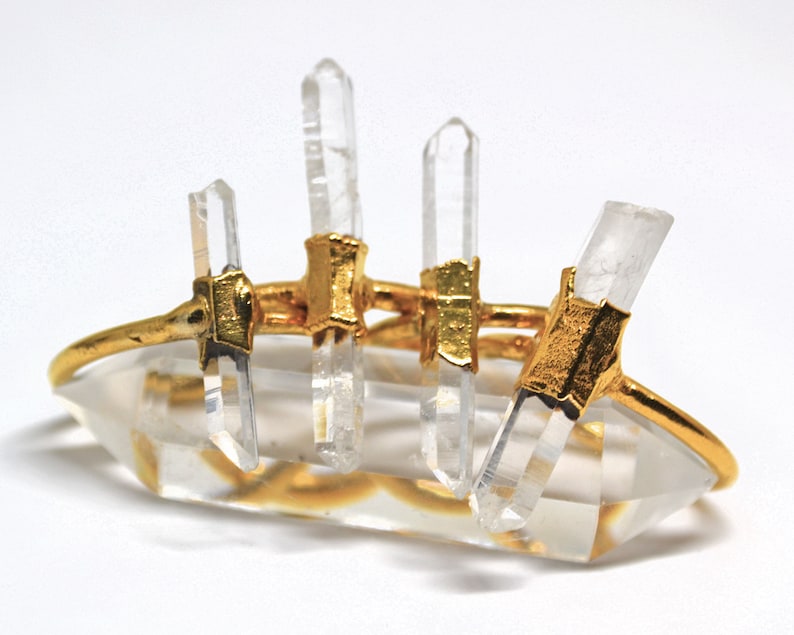 K&ouml;nnte beinhalten: Goldring mit f&uuml;nf klaren Quarzkristallen, die in Gold gefasst sind. Der Ring besteht aus einem d&uuml;nnen Goldband und die Kristalle sind so gefasst, dass sie aus dem Band herauswachsen scheinen.