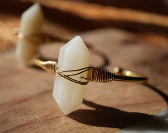 May include: A gold wire wrapped bracelet with a white crystal pendant. The bracelet is on a wooden surface.