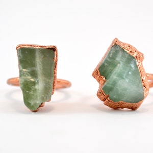 Op de afbeelding: Twee ringen met groene edelsteen bezettingen. De ringen zijn gemaakt van koper en hebben een ruwe, natuurlijke uitstraling.