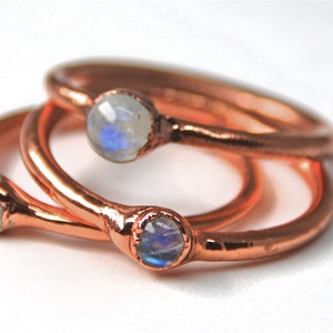 May include: Three copper rings with moonstone gemstones. The rings are stacked on top of each other.
