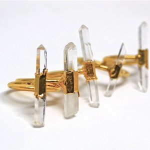 K&ouml;nnte beinhalten: Drei goldene Ringe mit klaren Quarzkristallspitzen. Die Ringe sind &uuml;bereinander gestapelt.