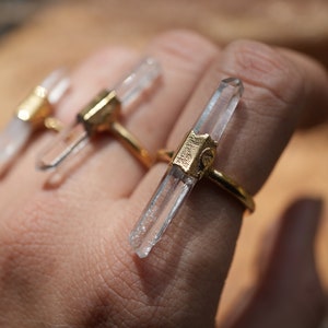 K&ouml;nnte beinhalten: Drei goldene Ringe mit klaren Quarzkristallspitzen. Die Ringe werden an einem Finger getragen.