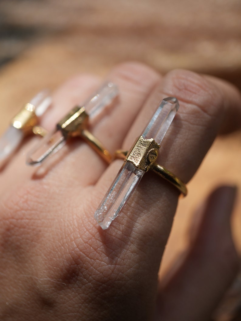 K&ouml;nnte beinhalten: Drei goldene Ringe mit klaren Quarzkristallspitzen. Die Ringe werden an einem Finger getragen.