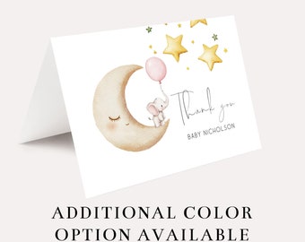 May include: A thank you card with a watercolor illustration of a baby elephant riding a crescent moon with a pink balloon. The elephant is holding onto the balloon with its trunk. There are three gold stars in the background. The text "Thank you" is written in cursive with the name "Baby Nicholson" below it.