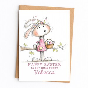 May include: Easter greeting card featuring a whimsical bunny illustration. The bunny wears a pink apron and a flower crown, holding a basket of Easter eggs. The card includes the text "HAPPY EASTER to our little bunny Rebecca."