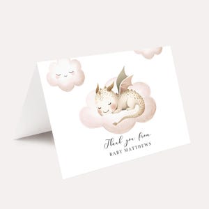 May include: A folded white card featuring a watercolor illustration of a sleeping baby dragon on a pink cloud. The dragon is cream-colored with brown accents and small wings. The text "Thank you from BABY MATTHEWS" is written in elegant script.