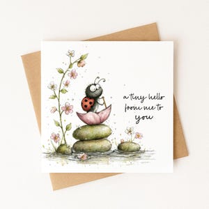 May include: A greeting card with a watercolor illustration of a ladybug on a stack of stones. The ladybug is holding a small stick and is perched on a pink lotus flower. The card has the text "a tiny hello from me to you".