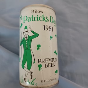 May include: A white metal beer can featuring green text that reads Bilow St. Patrick's Day 1981 Premium Beer. The can displays a graphic of a person in a green suit and top hat, surrounded by green shamrock illustrations. It holds 12 fl. oz. (355 ml).
