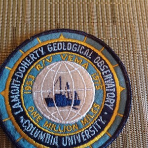 May include: A round patch with a blue border and gold accents. The patch features text that reads "Lamont-Doherty Geological Observatory" and "Columbia University." A globe and ship graphic are in the center.