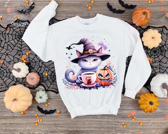 May include: White sweatshirt featuring a watercolor illustration of a gray cat wearing a witch hat, a teacup, and a jack-o'-lantern. The design includes purple, orange, and pink accents, perfect for Halloween. The sweatshirt is surrounded by pumpkins and Halloween decorations.