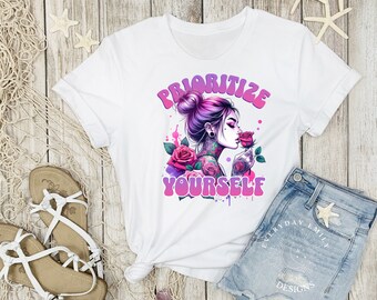 May include: White t-shirt featuring a graphic of a woman with purple hair and tattoos, smelling a rose. The text "PRIORITIZE YOURSELF" is in pink and purple. The shirt is paired with denim shorts and sandals.