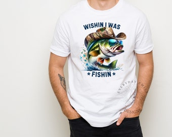 May include: White t-shirt with a graphic of a fish wearing sunglasses and a camouflage cowboy hat. The text on the shirt reads "Wishin I Was Fishin" with star accents. The design features blue, green, and brown colors.