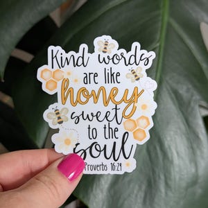 May include: A white sticker with the text "Kind words are like honey sweet to the soul" in black and yellow script. The sticker features illustrations of bees and honeycomb. The Bible verse Proverbs 16:24 is printed at the bottom.