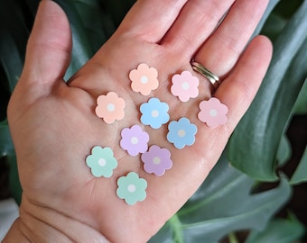 May include: A collection of pastel-colored flower stickers with white centers. The stickers are arranged in a hand, with the colors ranging from light pink to light blue.