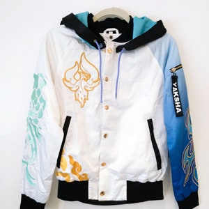 May include: A white bomber jacket with a black hood and a blue and white gradient on the right sleeve. The jacket has gold embroidery on the front and sleeves, including a phoenix design on the front. The zipper on the right sleeve has a "YAKSHA" tag.