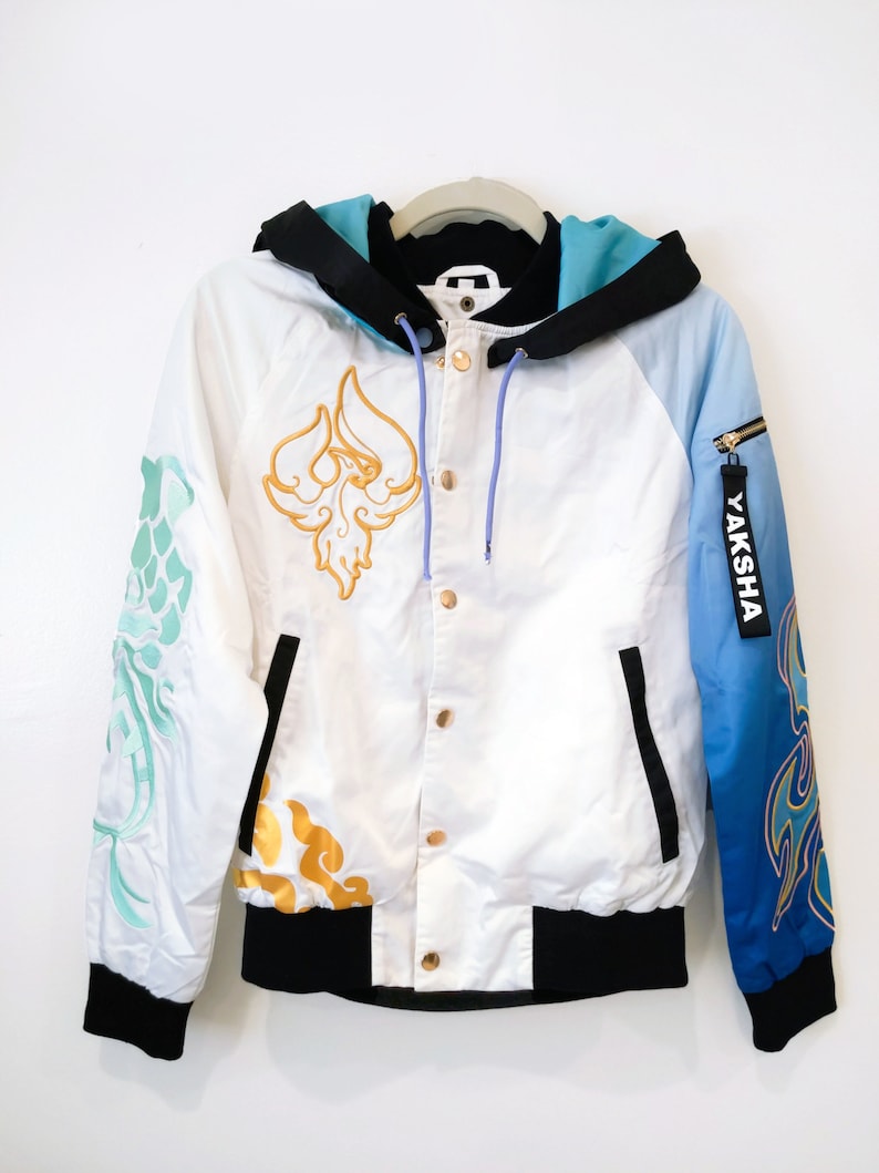 May include: A white bomber jacket with a black hood and a blue and white gradient on the right sleeve. The jacket has gold embroidery on the front and sleeves, including a phoenix design on the front. The zipper on the right sleeve has a "YAKSHA" tag.