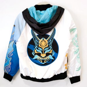May include: White hooded jacket with a blue and gold mask design on the back. The mask is in a circle with blue and white waves around it. The jacket has blue and white sleeves with a gold and white design.