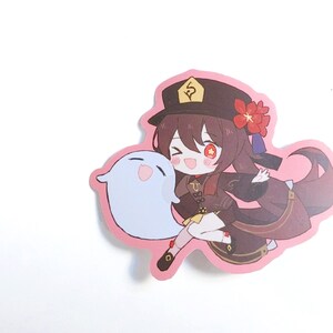 May include: A pink sticker featuring a cartoon character with brown hair, wearing a black hat with a gold symbol, a red flower, and a brown and gold outfit. The character is holding a white ghost with pink cheeks.