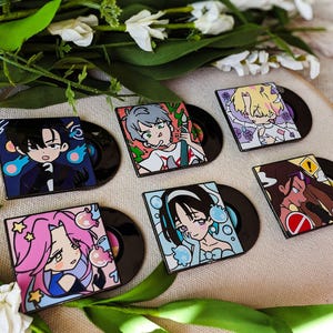 May include: Six square enamel pins featuring stylized anime-inspired character illustrations, each attached to a small black circular vinyl record base. The designs include various characters with distinct hair colors, expressions, and graphic elements.