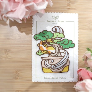 Op de afbeelding: Gestikt patch met een bonsaiboom met een koi-vis die in het water zwemt. Het patch is gelabeld met "Bonsai Tree Series" en "Embroidered Patch".