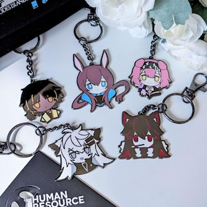 May include: A collection of anime-style keychains featuring various character designs. Each keychain has a black chain and a metal clasp. The keychains showcase characters with distinct hairstyles and outfits, in colors like brown, pink, and white.