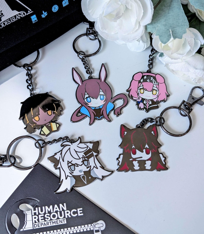 May include: A collection of anime-style keychains featuring various character designs. Each keychain has a black chain and a metal clasp. The keychains showcase characters with distinct hairstyles and outfits, in colors like brown, pink, and white.