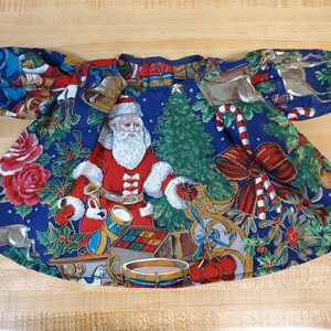 May include: A blue fabric doll dress with a Christmas theme. The dress features a Santa Claus, a Christmas tree, reindeer, and other holiday imagery.