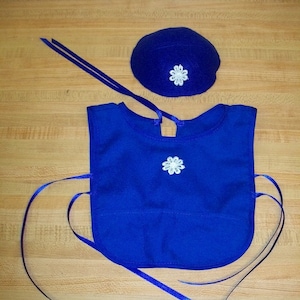 May include: A blue fabric bib with white lace trim and a matching blue fabric hat with white lace trim.