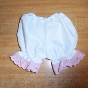 May include: White cotton bloomers with pink lace trim. The bloomers are gathered at the waist and have a ruffled edge.