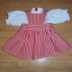 Puede incluir: Un vestido de rayas rojas y blancas con una blusa blanca y un botón de flor roja. El vestido tiene una falda fruncida y un corpiño ajustado.