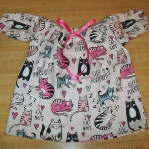 May include: A pale pink nightdress featuring a cat print, short sleeves, and a pink ribbon. The fabric is decorated with cat drawings, hearts, and the phrases "Sleep is Purrrfect" and "I love cat naps."