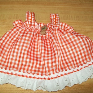 May include: Orange and white gingham doll dress with white lace trim and a brown button with a cat design.