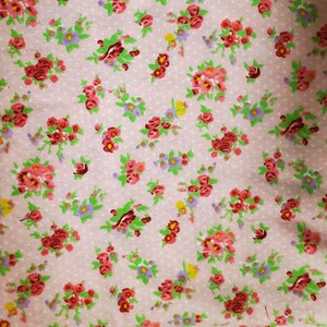 May include: A close-up of a pink fabric with a floral pattern. The pattern features clusters of red, pink, purple, and yellow flowers with green leaves. The background is a light pink with small white polka dots.
