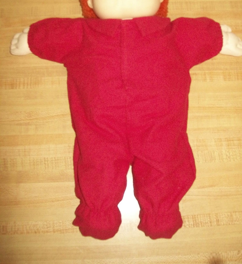 May include: A red doll wearing a red onesie with a collar. The doll has white hands and a white face. The doll has orange hair.