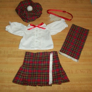 Könnte beinhalten: Ein rot-schwarzer karierter Rock mit weißem Fransenbesatz, eine weiße Bluse mit roter Schleife, ein rotes Stirnband und ein rot-schwarzer karierter Hut mit weißem Bommel.