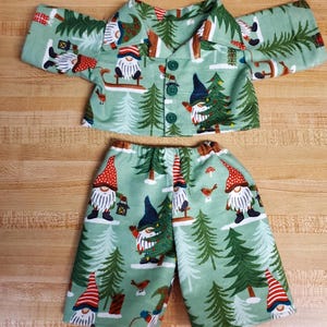 Pode incluir: Um conjunto de pijama verde e branco com um padrão de gnomo e árvore de Natal. A parte superior tem um colarinho com botões e mangas compridas. As calças são curtas com uma cintura elástica.